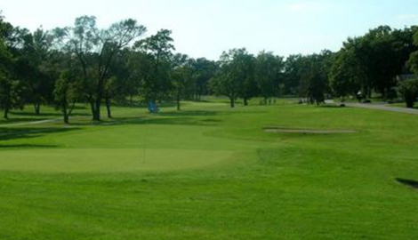 View of golf course with bunker to the right and blue flag over hole to the left